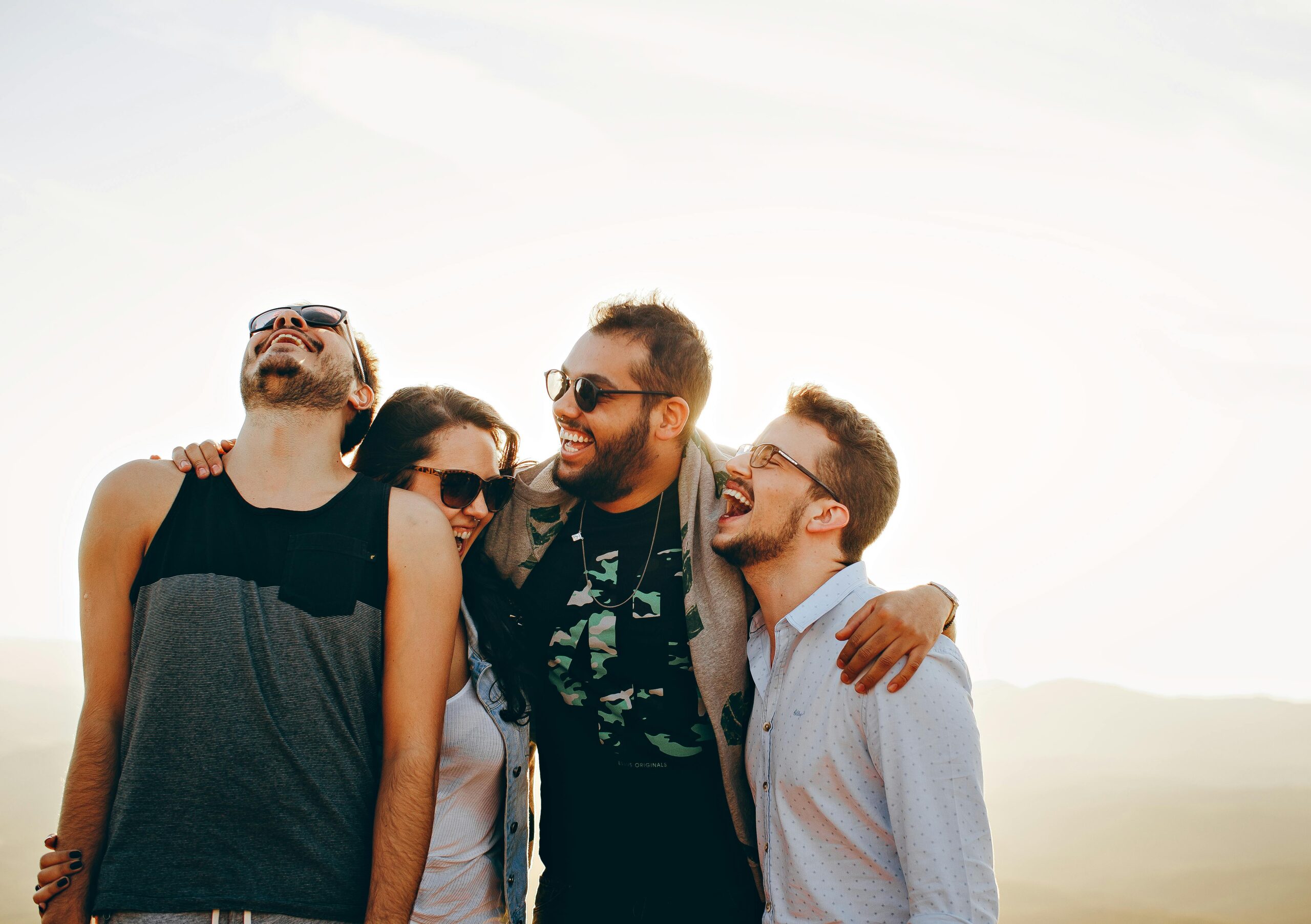 A group of young adults laughing and enjoying time together outdoors under the sun.